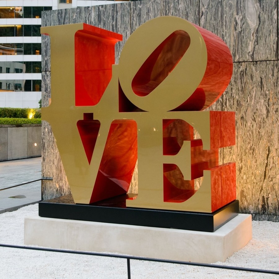 A 72 by 72 by 36 inch polychrome aluminum sculpture spelling love, consisting the letters L and a tilted letter O on top of the letters V and E. The faces of the letters are gold, and the sides are red.