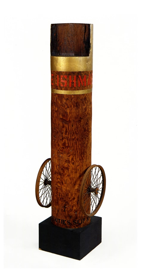 A 62 3/4 by 17 by 14 inch column with an iron wheel affixed on the bottom right and left sides, and standing on a wooden base. The top of the column is painted gold. Below, wrapping around the column, is the work's title, "Call Me Ishmael," painted in red letters. Below the text a thin gold stripe wraps around the column.