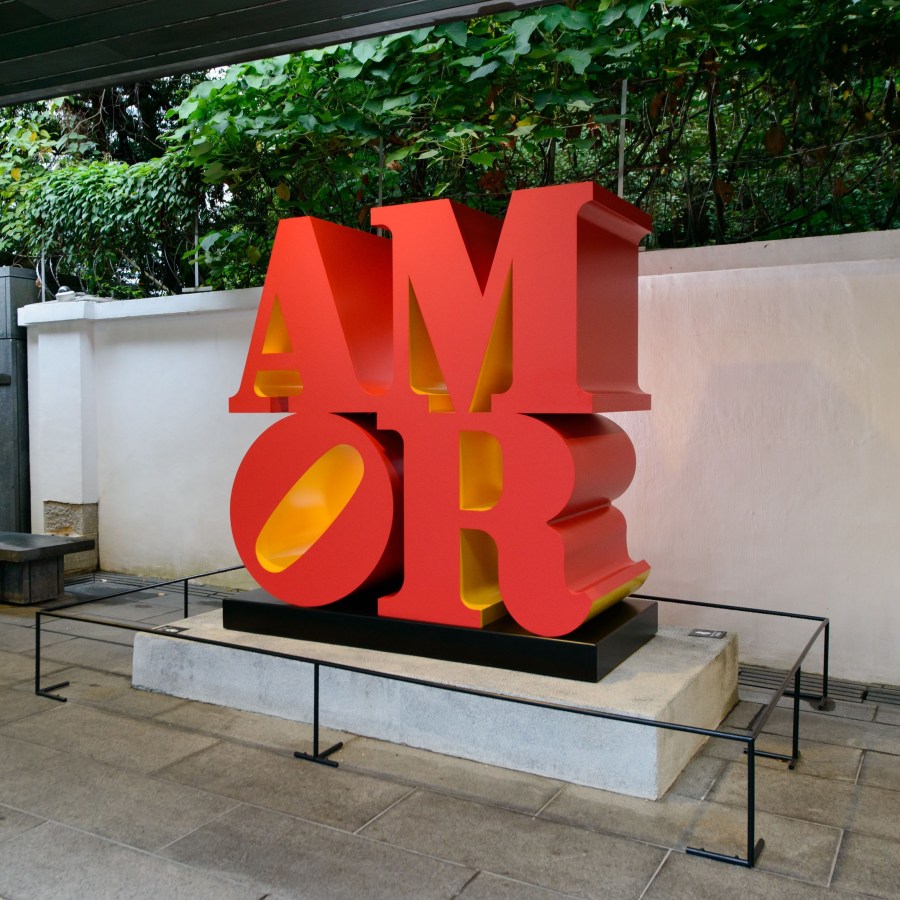 AMOR is a 72 by 72 by 36 inch polychrome aluminum sculpture consisting of the letters A and M atop a tilted O and R. The front, back and sides of the letters are red, and the insides are yellow.
