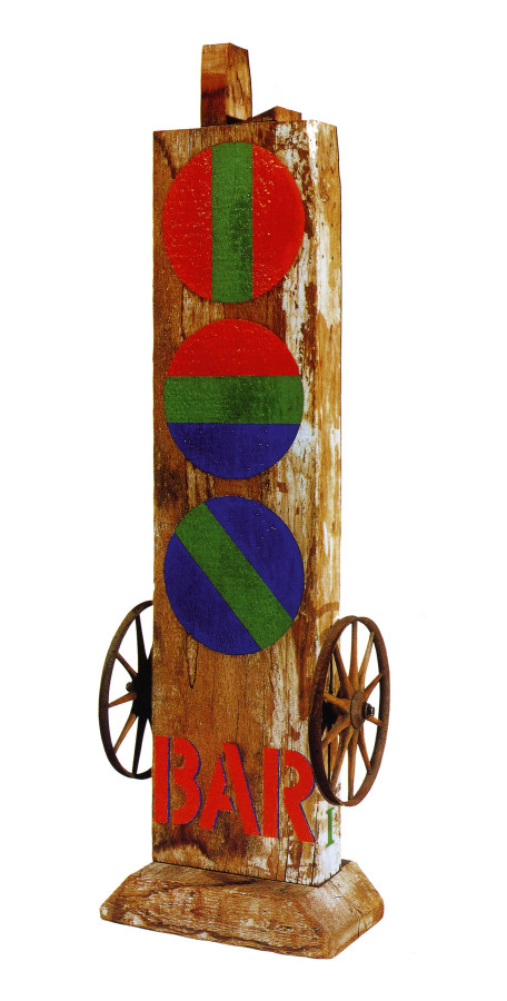 A sculpture consisting of a wooden beam with a haunched tenon, on a wooden base. The sculpture's title, "Bar," is painted in red stenciled letters across the bottom front of the work. Occupying the space from few inches above the title to the top of the sculpture are three painted red circles. The top one is red with a green vertical stripe down the center, the middle one consists of red, green and blue horizontal fields, and the bottom one is blue with a diagonal green stripe down the middle. An iron wheel has been affixed to the right and left sides of the sculpture, just above the title.