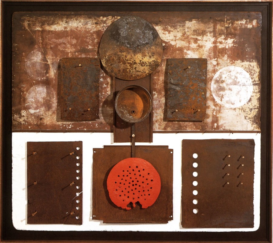 A wall construction; three flat rectangular metal pieces have been affixed on the bottom half of the work, which has been painted white. A circular red metal piece has been affixed on top of the central rectangular piece. Three smaller flat rusted rectangular pieces have been affixed in the top half of the work, and the central rectangular element contains a conical chimney cap at the top and a found metal container in the center. Two faded white orbs appear to the left of the metal elements, and one white orb to the right.