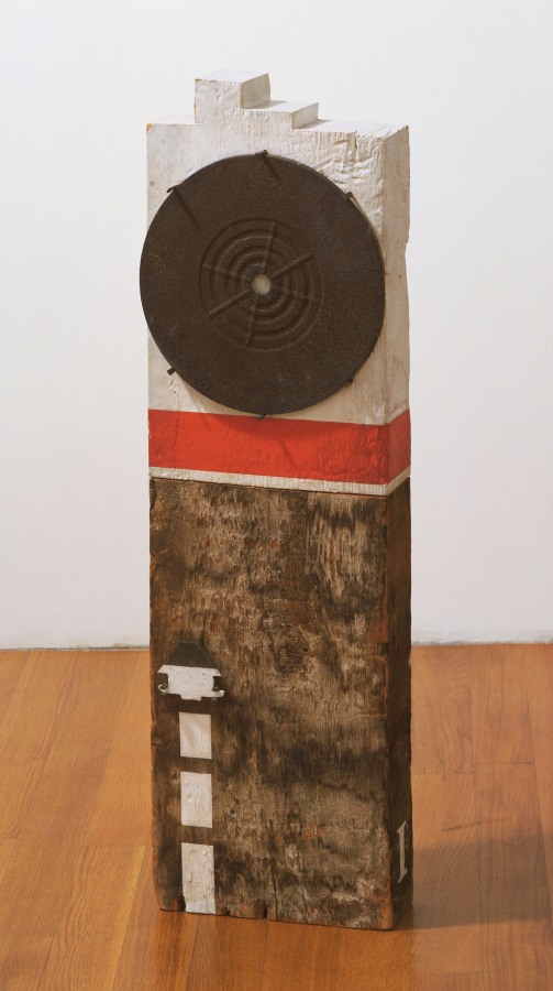 A sculpture consisting of a wooden beam with a tenon. The top half of the sculpture has been gessoed, the bottom half has been left bare with the exception of four small rectangular white shapes painted in a vertical line from the bottom left halfway up the bare portion of the work. A red band has been painted on the lower part of the gessoed half, and above it is a circular metal disk.