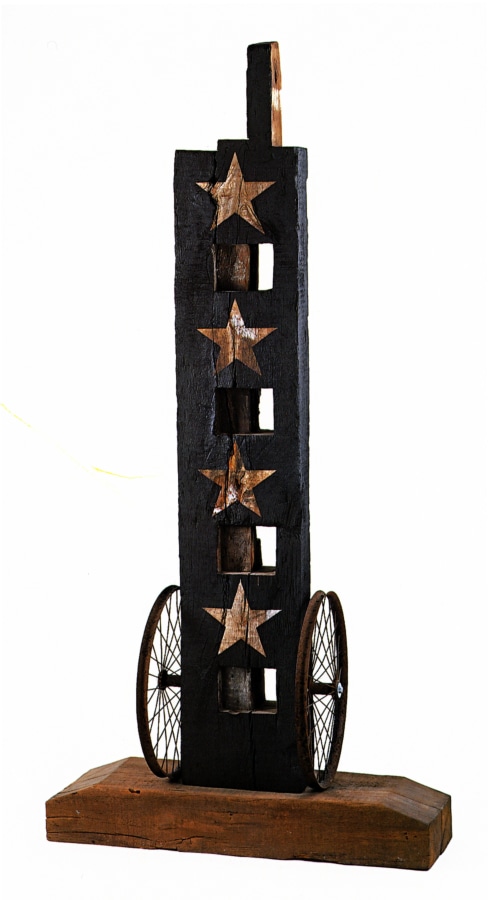 A 74 1/2 by 36 3/4 by 18 inch sculpture titled Four Star consisting of a wooden beam with a haunched tenon on a wooden base. An iron wheel is affixed to the bottom right and to the bottom left sides of the sculpture. The beam has been painted black except for four vertical stars on the front of the sculpture, which expose the natural wood. 