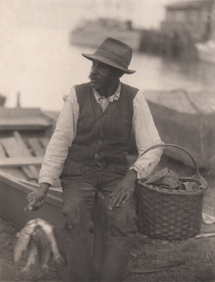 Doris Ulmann, Untitled (Fisherman),  ​1928–1934. Man seated on the bow of a small fishing boat holding a basket and fish.