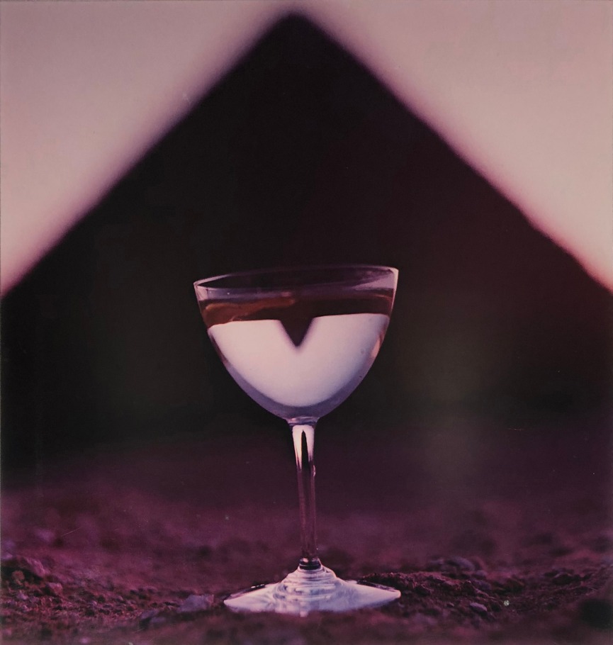 Bert Stern, Martini & Pyramid, for Smirnoff Vodka, ​1955. Martini glass on sand with a triangle shape out of focus in the background.