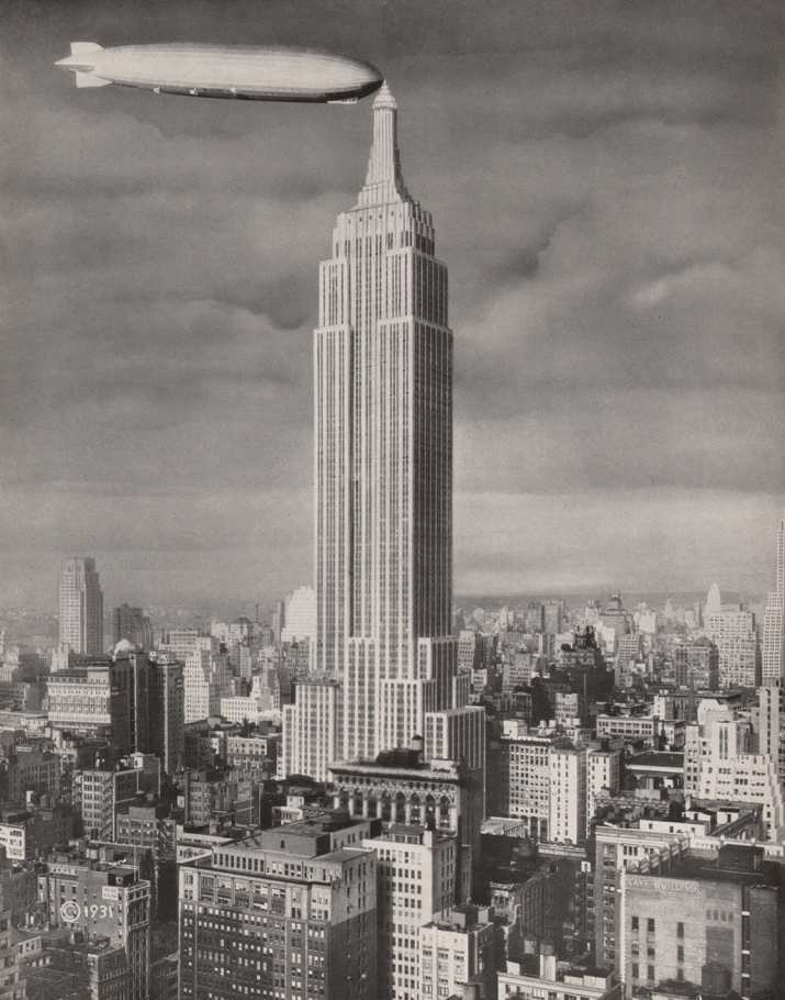 City skyline with the towering Empire State Building in center frame. A dirigible is docked on the left at the highest point of the building.