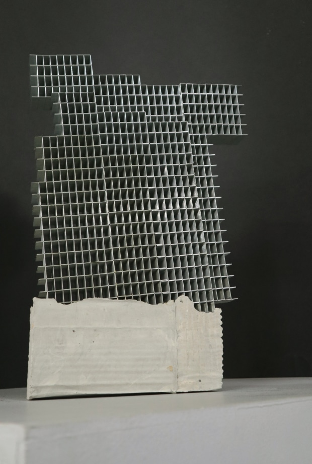 Sculpture of a building made of staple pins on cement block.