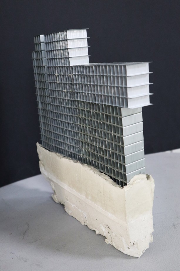 Sculpture of a building made of staple pins on top of cement block