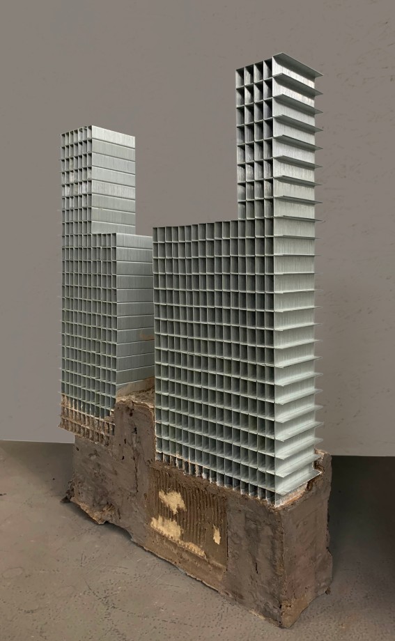 Sculpture of a building made of staple pins on cement block.