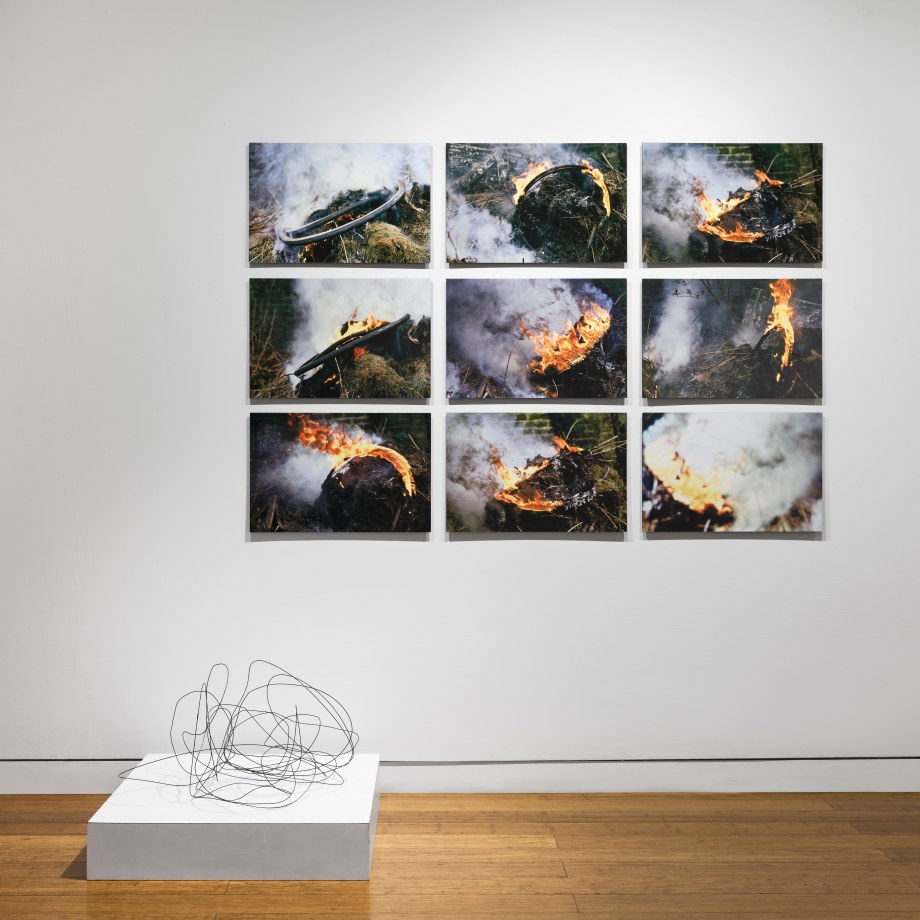 Art installation with 9 photographs of burning bicycle tyres and a floor sculpture of the burnt wire rims