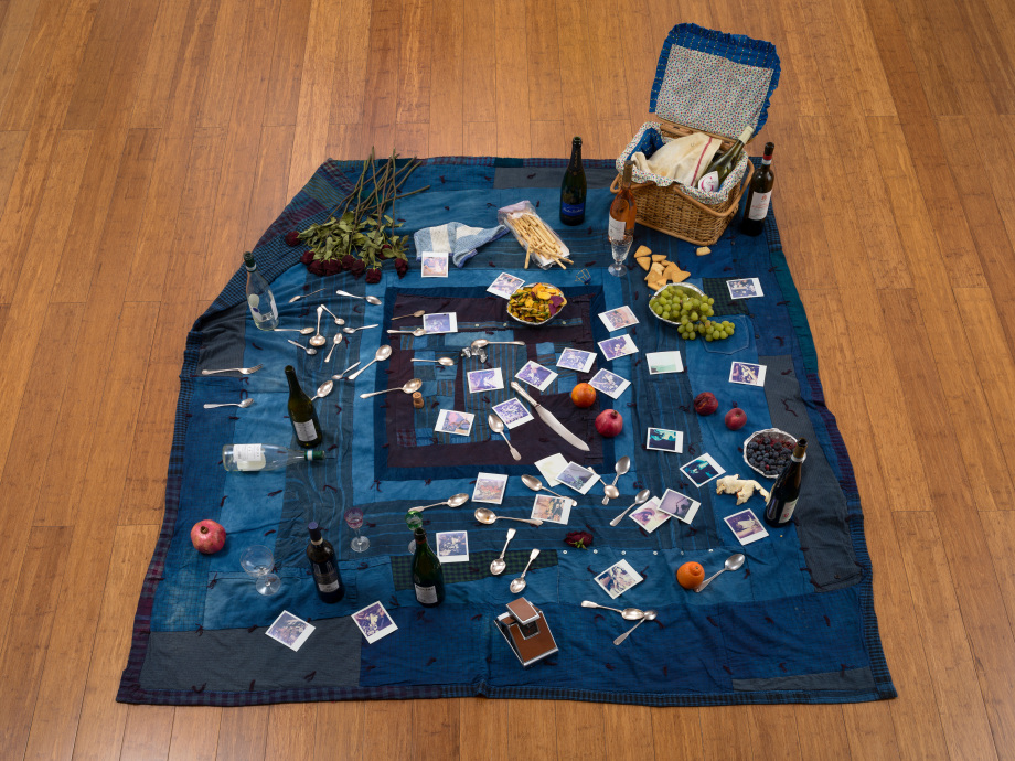 Bhasha Chakrabarti + Thew Smoak, Heartbreak Picnic, 2022-25 Installation using picnic basket, used clothing quilt, Polaroids, crystal, silverware, wine bottles, and seasonal fruit, Dimensions variable, CHABH001