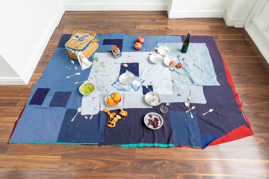 Bhasha Chakrabarti + Thew Smoak, Heartbreak Picnic,&nbsp;2022-25&nbsp;Installation using picnic basket, used clothing quilt, Polaroids, crystal, silverware, wine bottles, and seasonal fruit,&nbsp;Dimensions variable, CHABH001