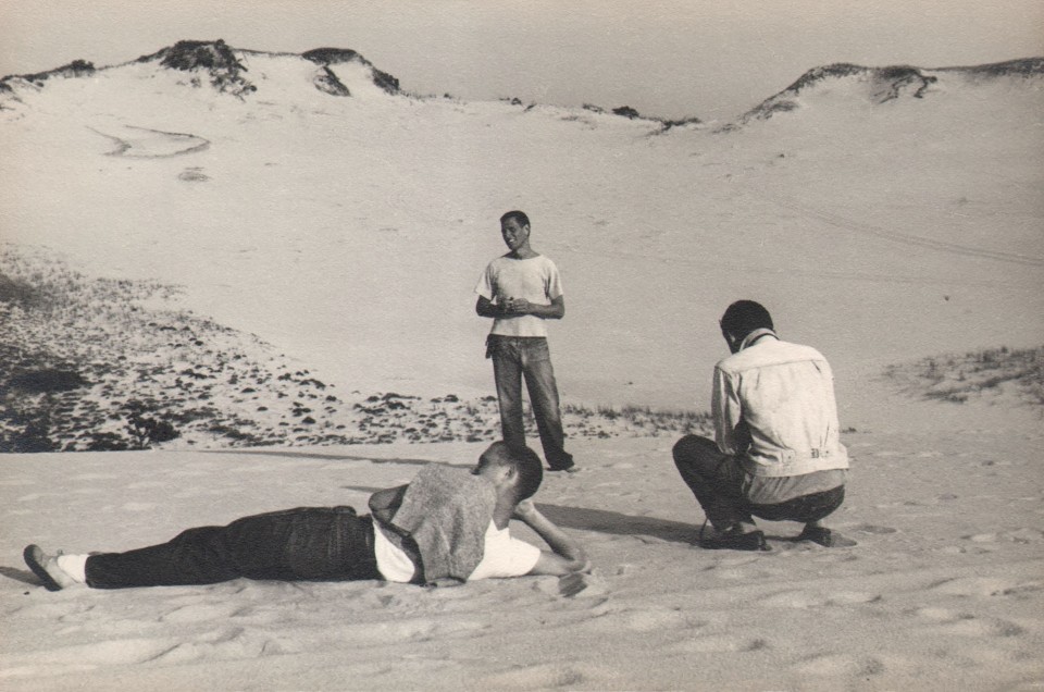 PaJaMa, George Tooker, Paul Cadmus, William Caskey, Provincetown, ​c. 1945. Three figures on a beach; one laying down (left), one standing (center), and one crouched (right).