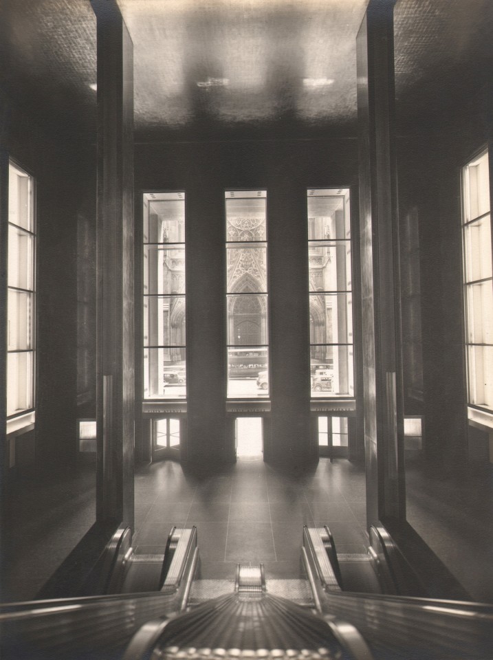 Paul J. Woolf, International Building Lobby, ​c. 1935. Lobby with tall windows photographed from between the top of two escalators. Cathedral entrance opposite can be seen through center window.