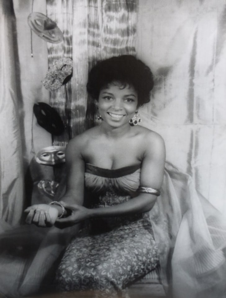 39. Carl Van Vechten, Ruby Dee, 1962. Seated portrait with subject smiling to the camera, adjusting a bracelet on her wrist. Backdrop features draping fabric and masks.