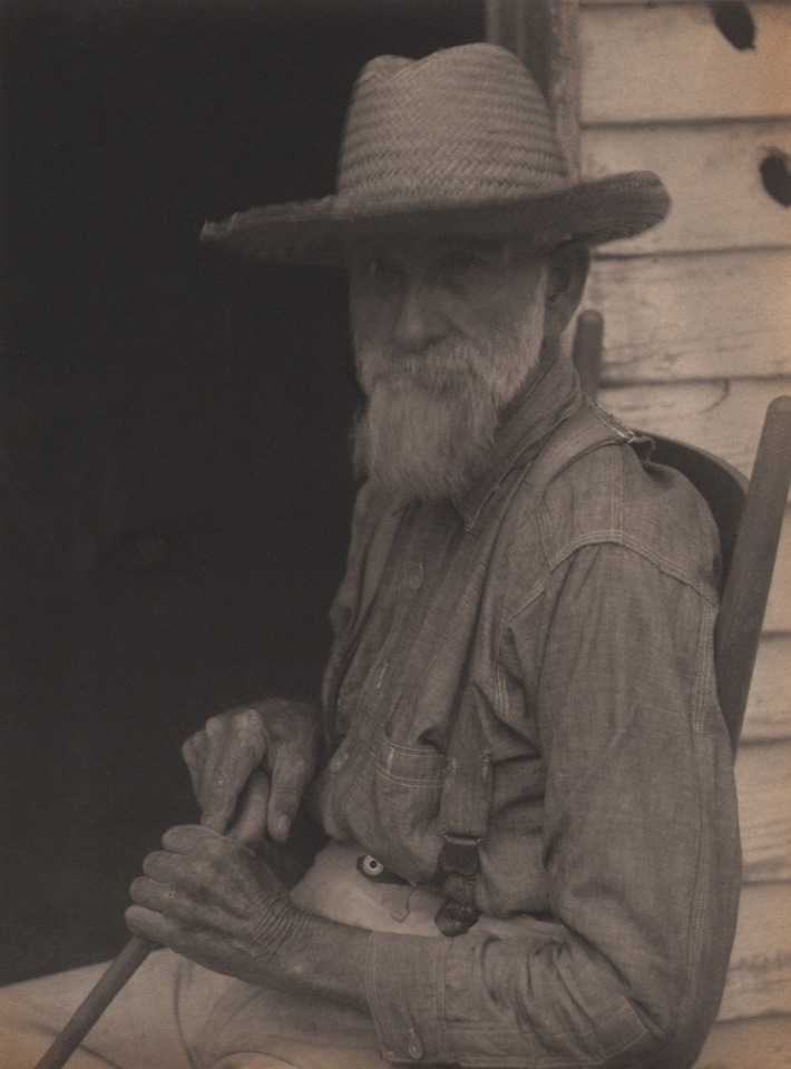 Doris Ulmann, Untitled (Farmer), 1928&ndash;1934. Older man in suspenders and straw hat seated on a wooden chair, holding a cane,