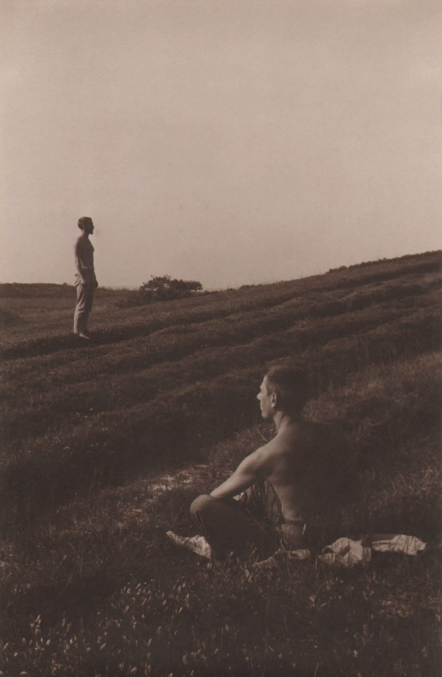 PaJaMa, George Tooker, Paul Cadmus, Nantucket, ​1946. Shirtless figure seated in the foreground, facing left. Standing figure in the midground, facing right. Setting of rolling, grassy hills.