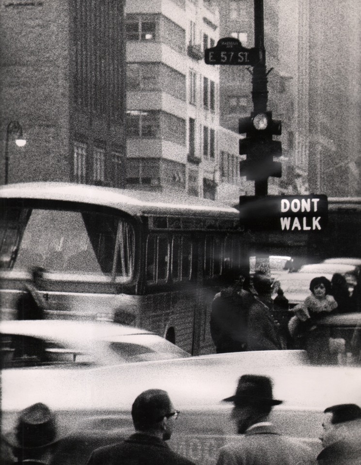 28. David Attie, Untitled, ​c. 1965. Street scene featuring a traffic light, crosswalk signal that reads &quot;Don't Walk,&quot; a sign reading &quot;E 57 St&quot;, vehicles, and a number of pedestrians.