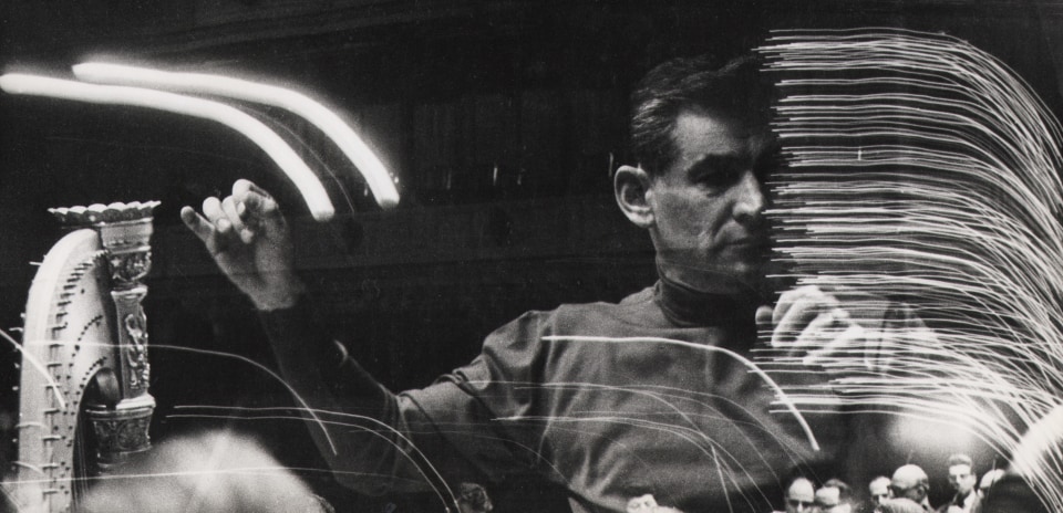 06. David Attie, Leonard Bernstein, rehearsal at Carnegie Hall, ​1959. Multiple-exposure photograph featuring a man with arms raised as if conducting and streaks of light.