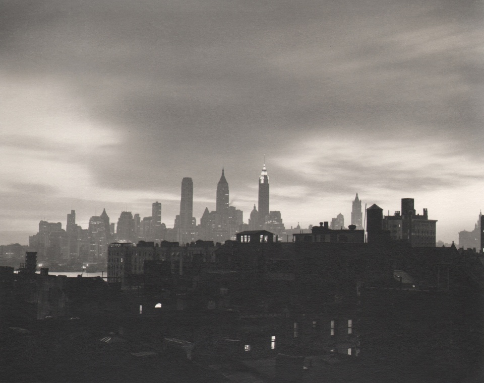 35. John C. Hatlem, New York City Skyline, ​c. 1935. Dark, mostly silhouetted view of the city from across a river. Dark buildings in the foreground. The Empire State is in the center background against a cloudy sky.