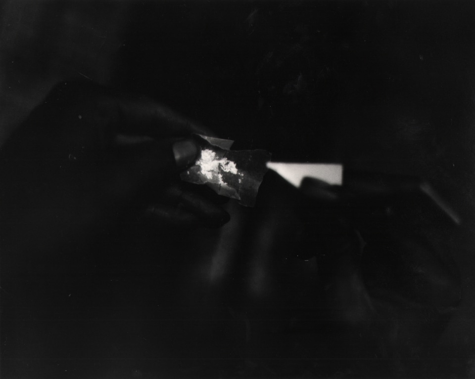 19. Shawn Walker, Drugs, Essence Magazine, ​1960s. Very dark photograph of a hand holding a small, opened packet of white powder.