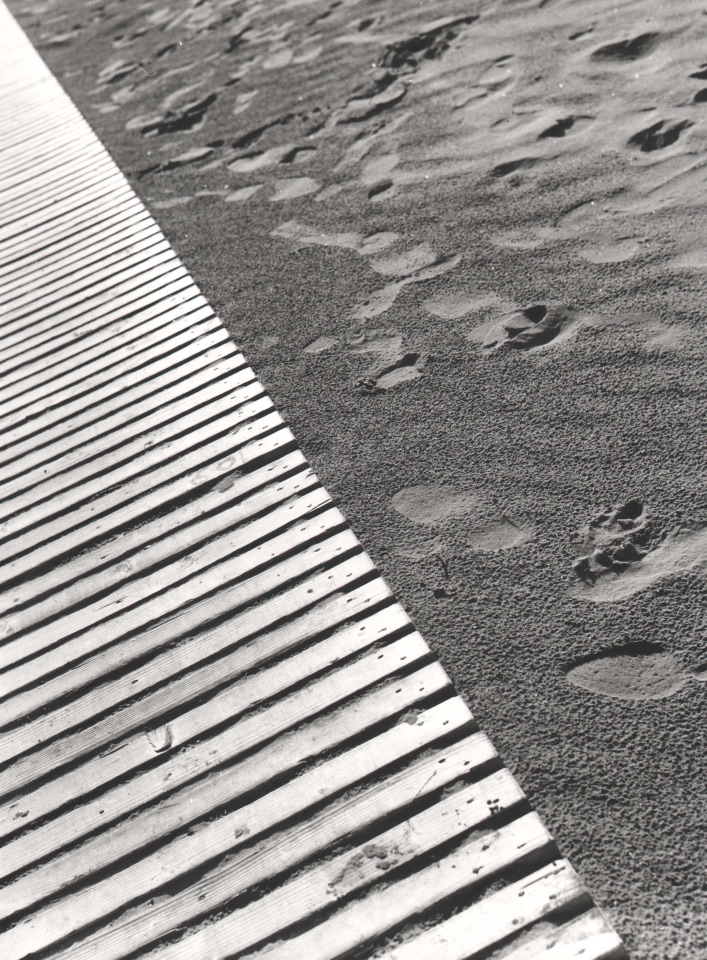 Nino Migliori, Untitled, 1951. Frame is diagonally divided; one half is a wooden dock, the other footprints in the sand.