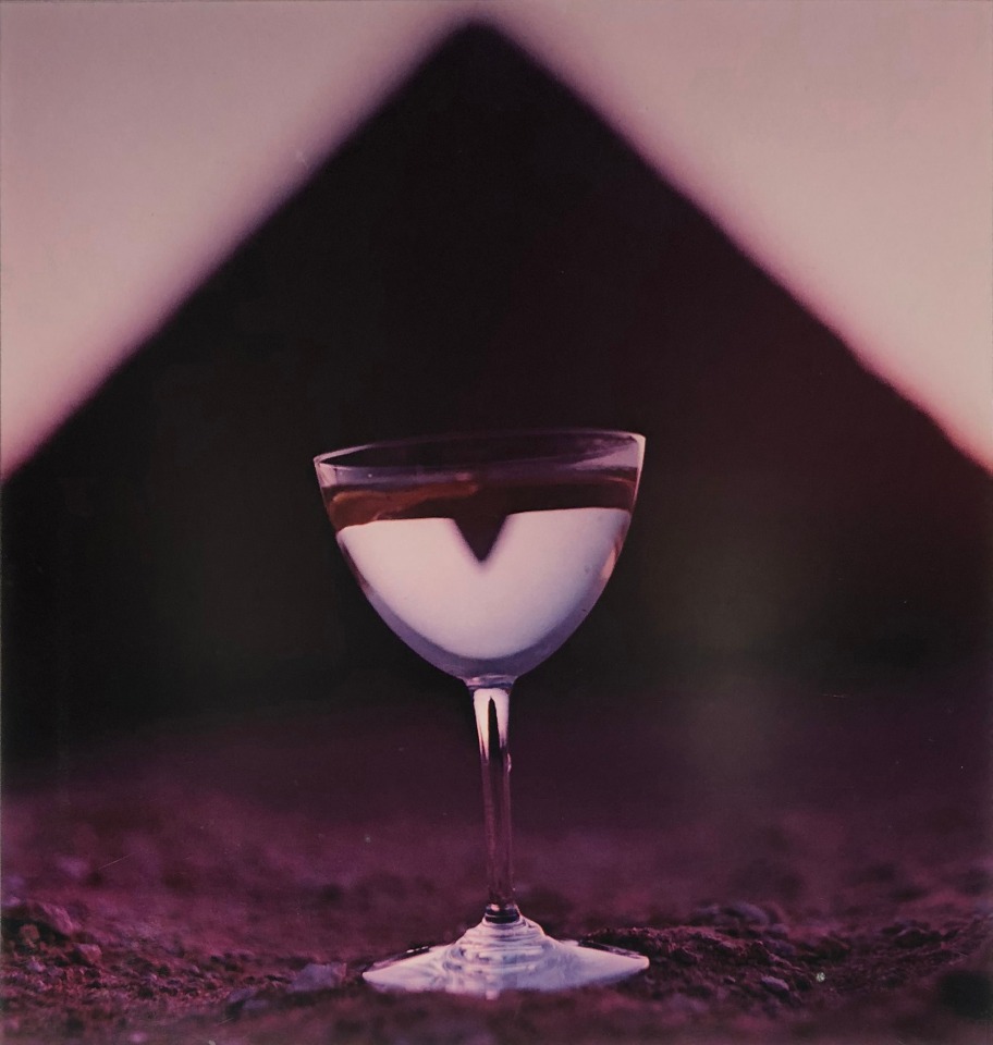 Bert Stern, Martini &amp; Pyramid, for Smirnoff Vodka, ​1955. Martini glass on sand with a triangle shape out of focus in the background.