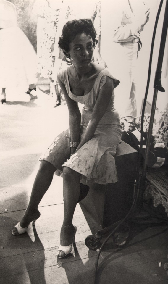 Bob Willoughby, Dorothy Dandridge, ​c. 1955. Subject is seated on a wooden crate backstage on film set, looking to the right.