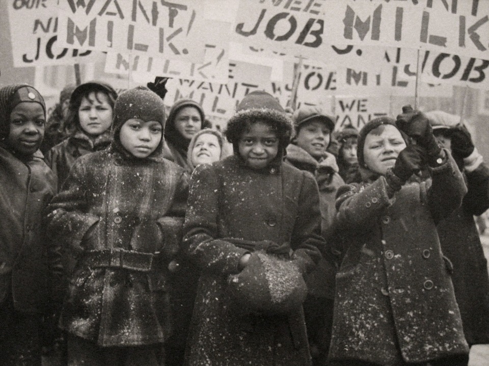 18. Gordon Coster, Untitled, ​c. 1938. Crowd of children in winter coats holding signs above their heads. Signs are in partial view, but the words &quot;MILK&quot; AND &quot;JOB&quot; can be seen.