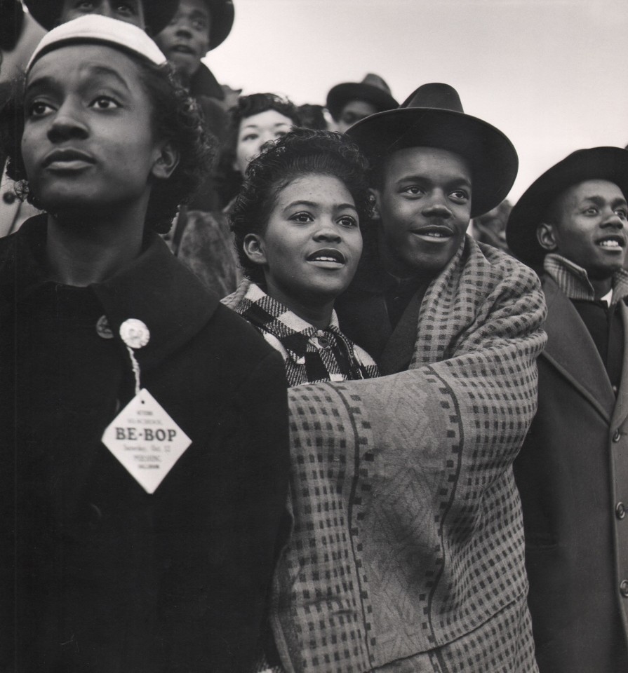 Wayne Miller, High School Football Game, Chicago, ​1946&ndash;1947. A large group of teenagers. A couple embraces with a blanket wrapped around them. Another teen in the foreground wears a &quot;Be-Bop&quot; pin.