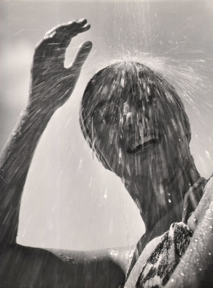 Stanislao Farri, Estate, ​1959. A woman smiles with eyes closed and one hand above her as water pours down onto her head.