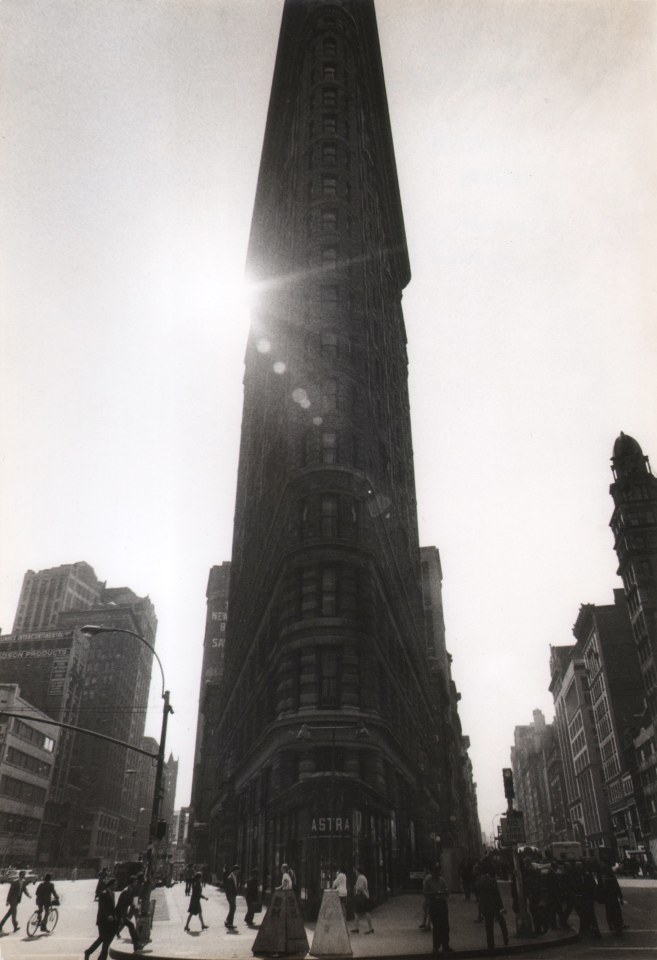 4B. Jan Lukas, Flatiron Building, 1966. Frontal view of the building mostly in silhouette, with sun streaks and spots shining from behind the top left corner of the building.