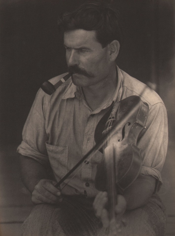 Doris Ulmann, Untitled (Fiddler), ​1928&ndash;1934. Seated man with pipe in his mouth, positioned to play the fiddle held against his left shoulder.