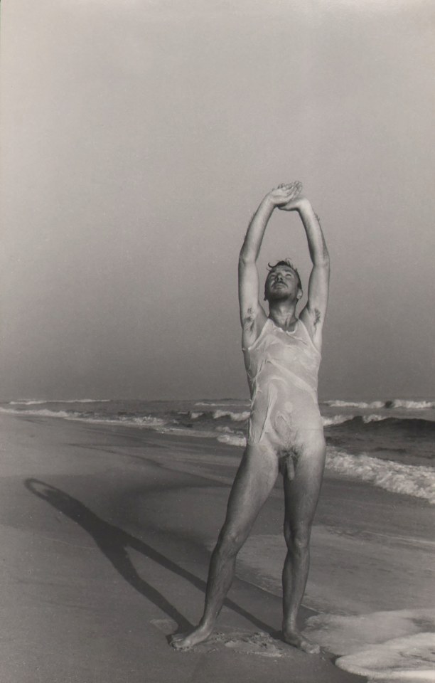 PaJaMa, Jared French, Saltaire, ​c. 1945. Male nude save for a thin white shirt stands in the foreground, reaching and looking upward, waves crashing behind him.