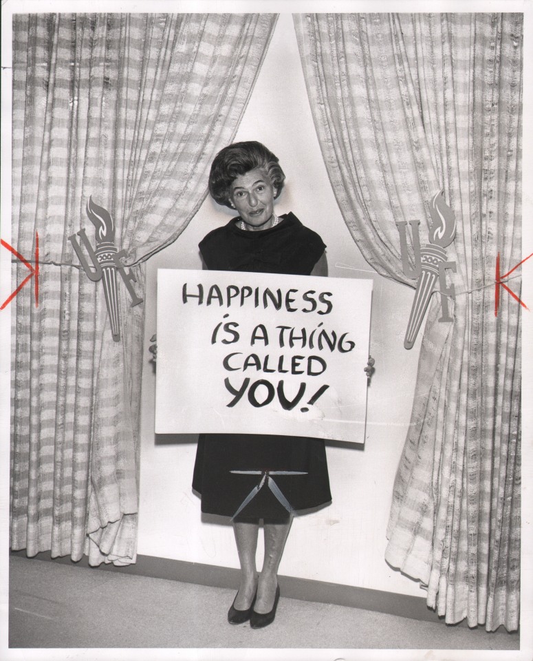 50. Anonymous, Untitled, ​1965. A woman stands between two curtains holding a sign that reads &quot;Happyiness is a thing called you!&quot;