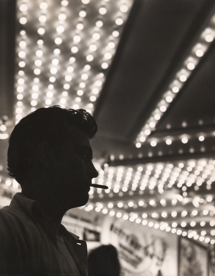 40. Benn Mitchell, Times Square, ​1950. Silhouette profile of a man with a cigarette in his mouth beneath rows of lights.