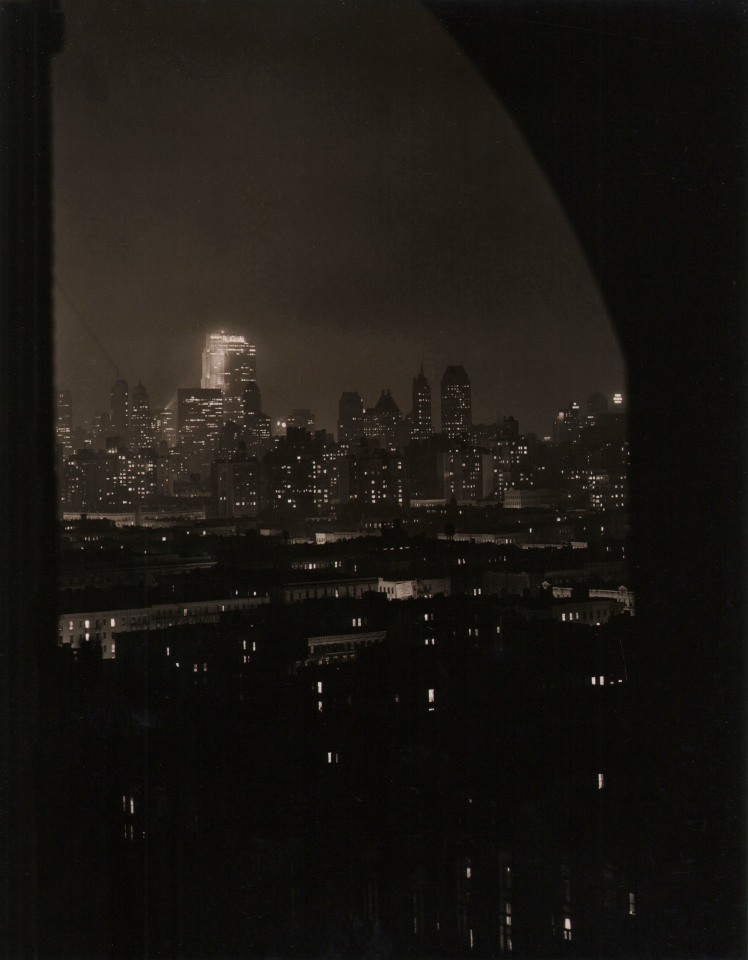 Paul J. Woolf, Rockefeller Center Looking South, ​c. 1935. Night time cityscape photographed from beneath a dark arch.