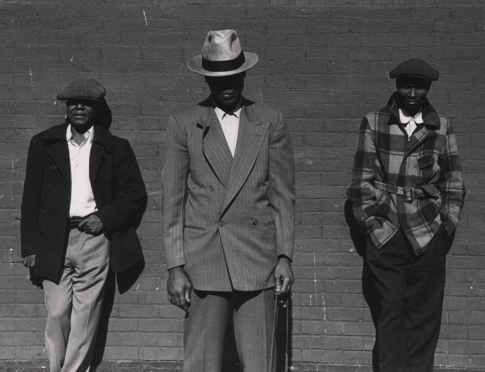 Marvin E. Newman, Chicago, ​1950. Three young adult men in hats and jackets pose against a brick wall. The central figure stands closer to the camera.