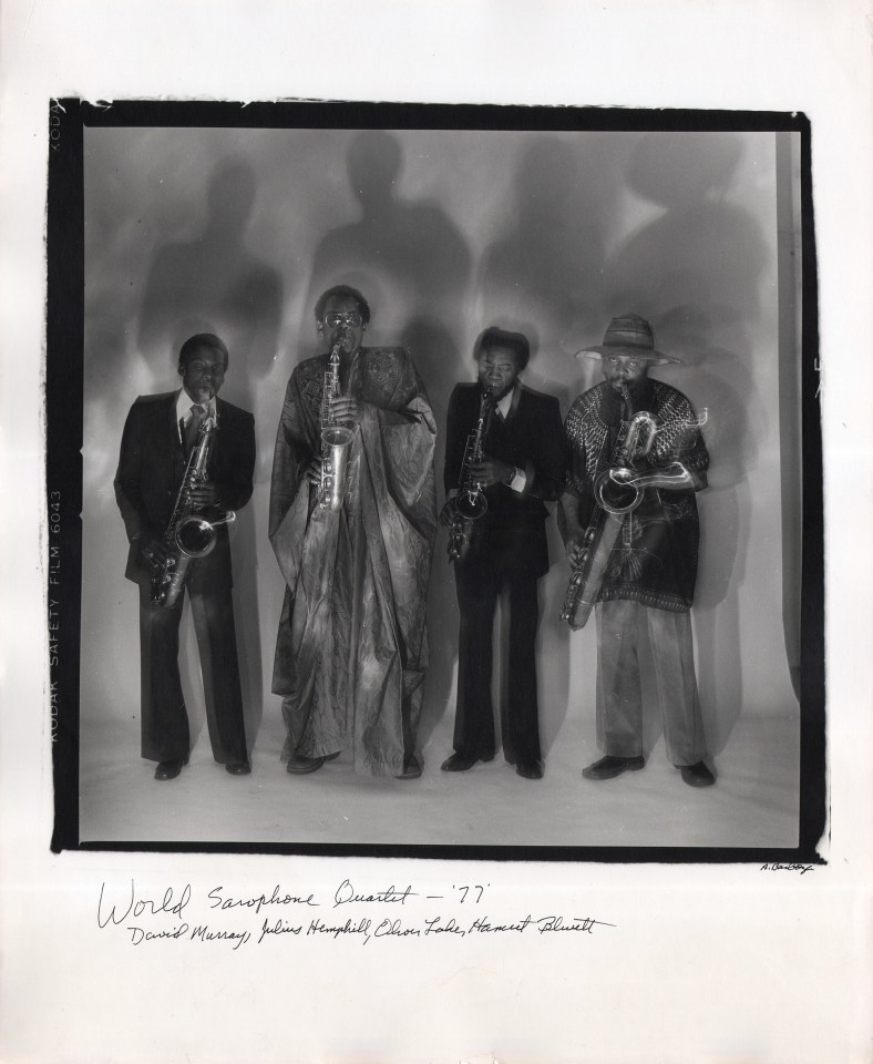 Anthony Barboza, World Saxophone Quartet - David Murray, Julius Hemphill, Oliver Lake, Hamiet Bluiett, ​1977. Four men stand across the square frame holding saxophones to their mouths, shadows cast up against the backdrop.