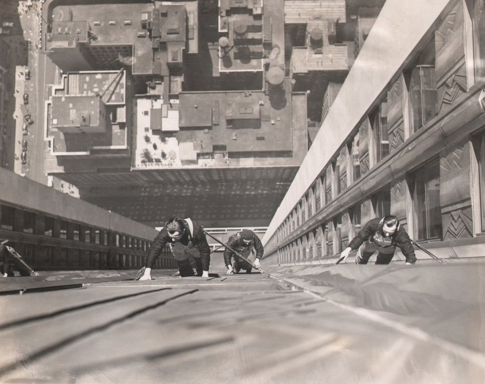 16. Wide World Photos, Human Flies as Window Cleaners, ​1938. Downward-looking view of three men suspended against the building facade with the city visible far below and behind them.