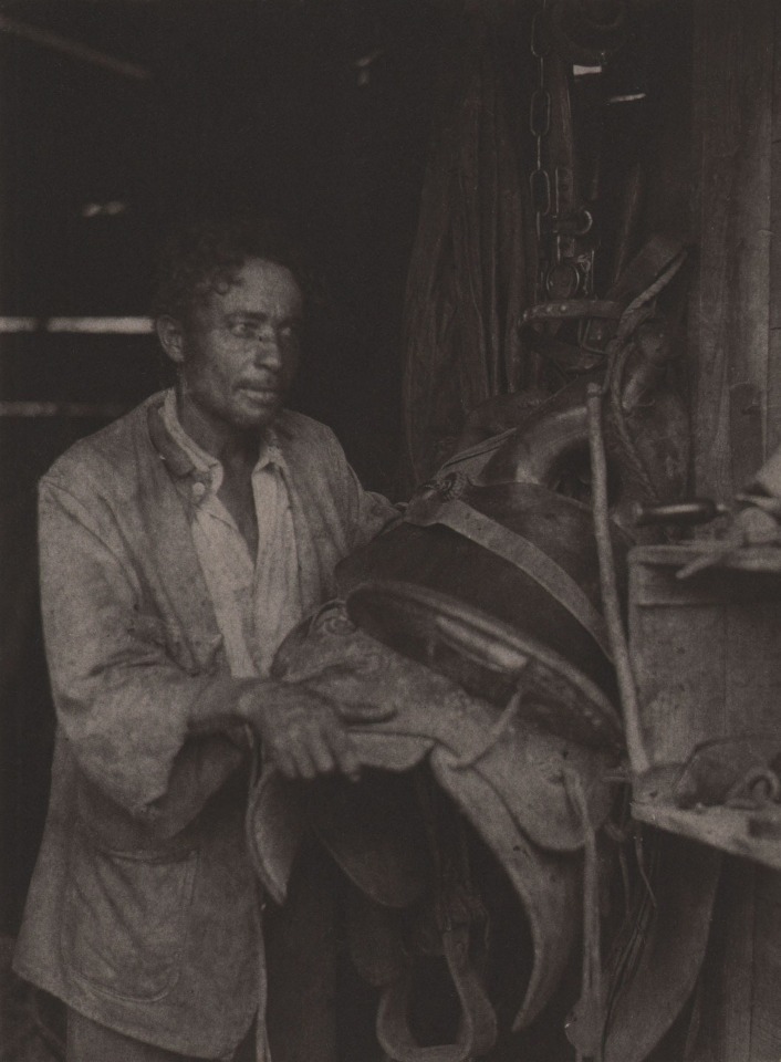 Doris Ulmann, Untitled (Horse handler), ​1928&ndash;1934. Man stands in a dark stable holding a horse's saddle.