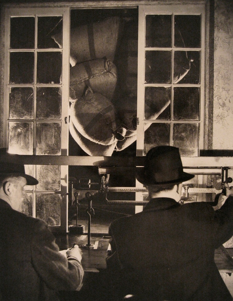 Harold Haliday Costain, Edgewater, NJ Sugar Refinery, 1935. Two men operate a scale with sacks of sugar in the background.