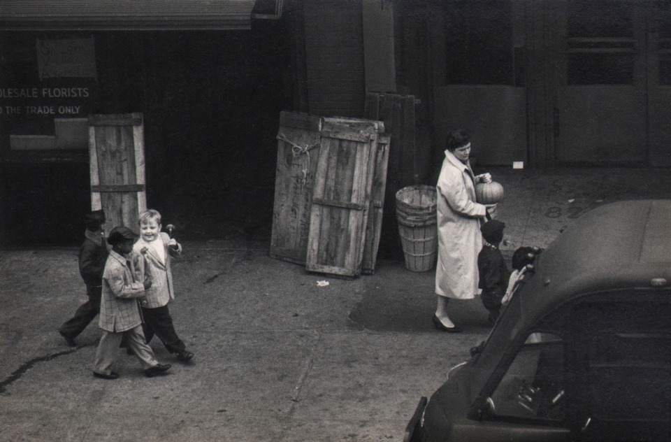 43. W. Eugene Smith, As From My Window I Sometimes Glance, ​1957&ndash;1958. A woman and four children carry a pumpkin and flowers on the sidewalk.