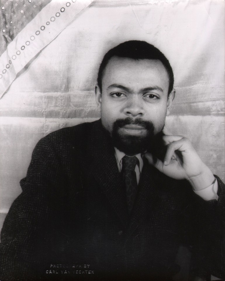 28. Carl Van Vechten, Amiri Baraka, 1962. Bust-length portrait of subject looking to camera against a cloth backdrop with chin resting on one hand.