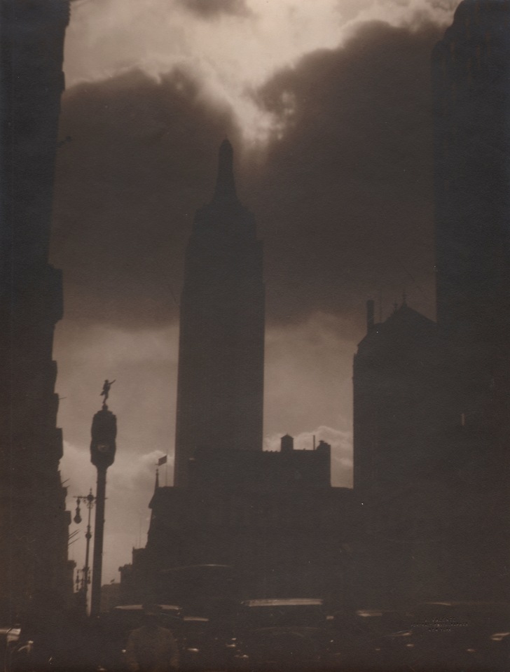 31. Alfredo Valente, Empire State Building, c. 1933. Sepia tone street view of silhouetted Empire State Building against a cloudy sky.