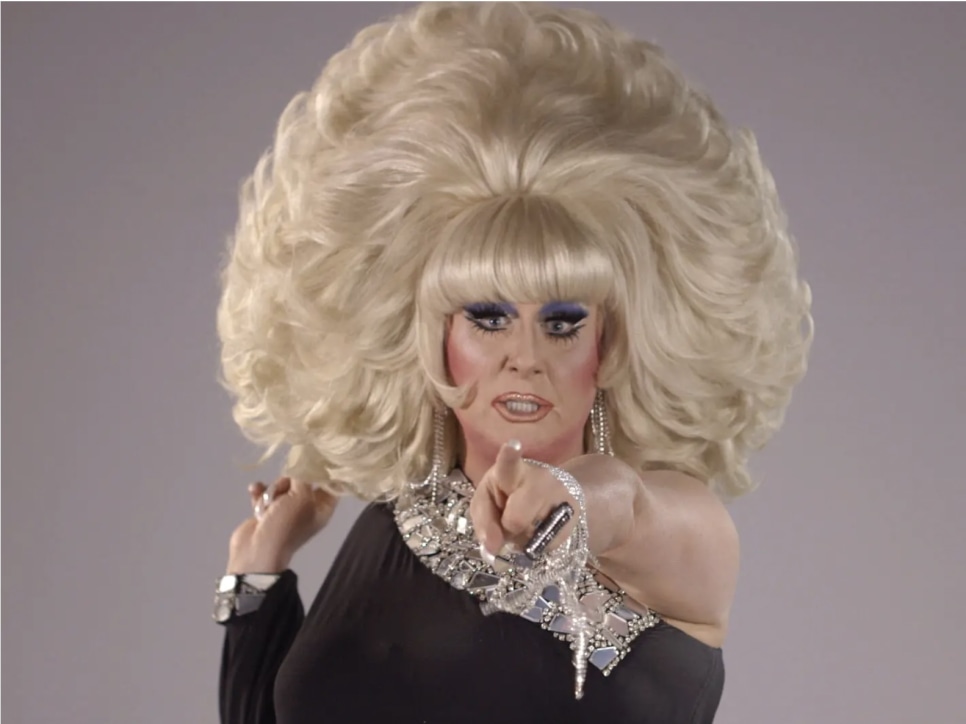 The drag performer Lady Bunny pointing at the camera, wearing a large blonde wig and black dress