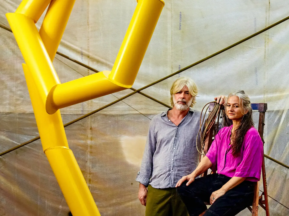 A man and woman next to a large yellow tubular sculpture
