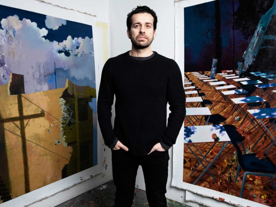 Man standing between 2 paintings of landscapes and buildings