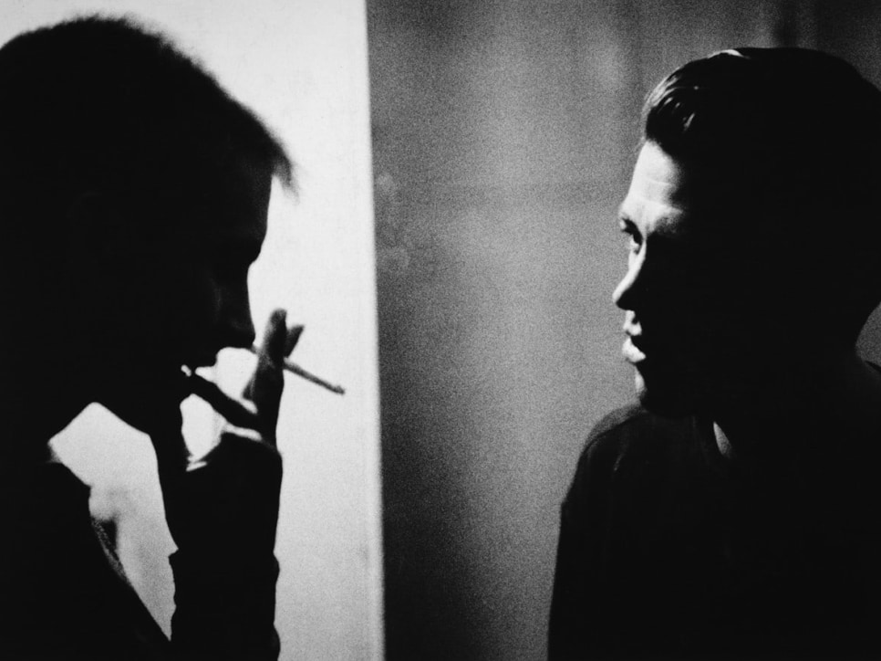 Black and white photograph of 2 men in conversation in a dark room