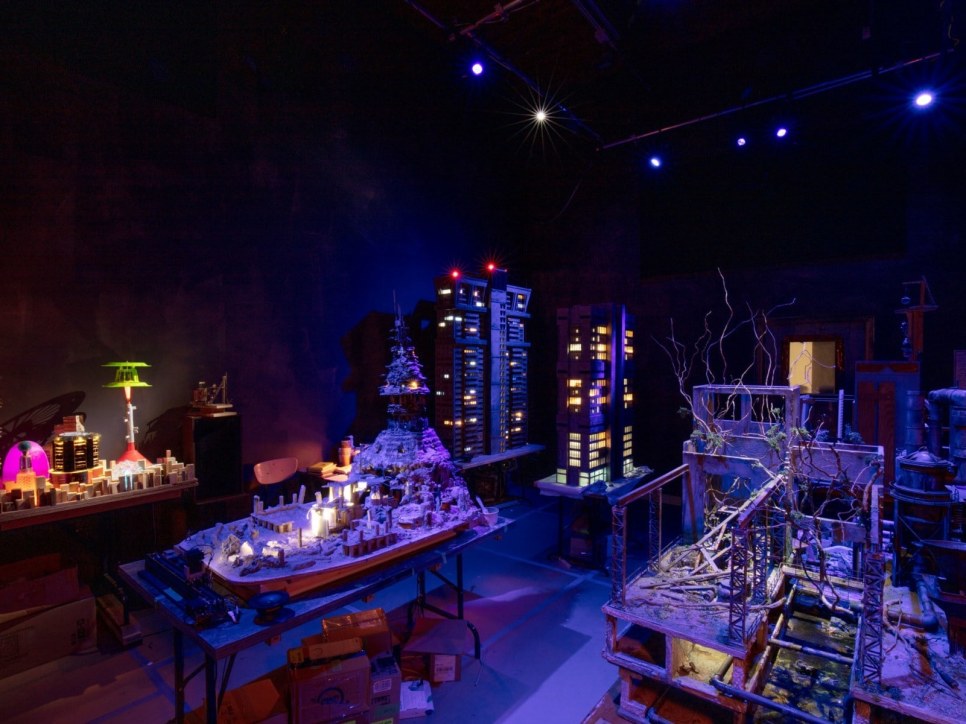 Gallery installation of a miniature city bathed in dark blue light